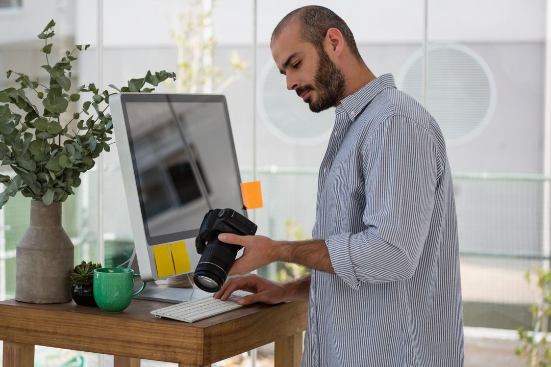Designer examining camera while standing by computer - Free Images, Stock Photos and Pictures on Pikwizard.com