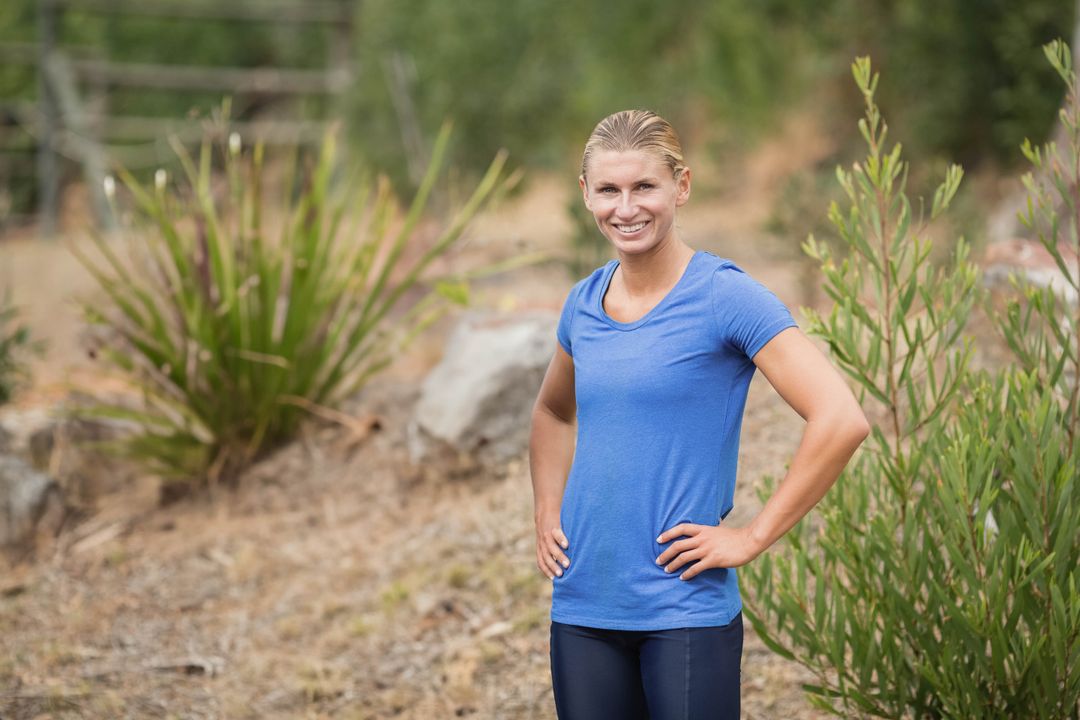 Fit woman smiling hands on hips on dry trail wearing bright blue top for outdoor fitness