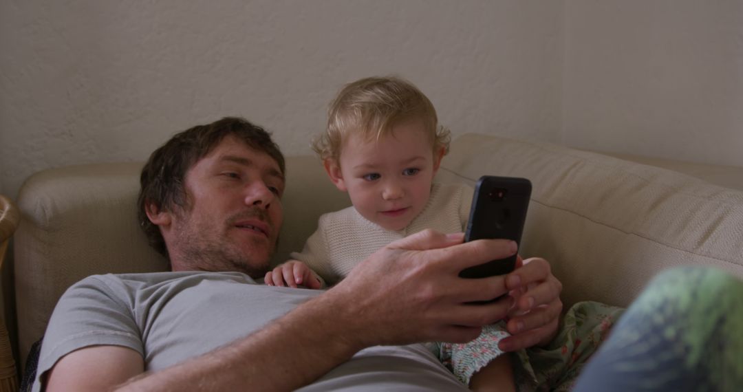 Father and toddler bonding on couch looking at smartphone - Free Images, Stock Photos and Pictures on Pikwizard.com