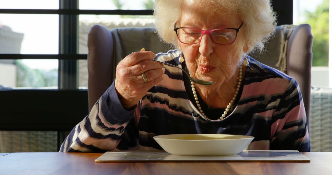 Elderly woman eating soup at home in sunny dining room - Free Images, Stock Photos and Pictures on Pikwizard.com