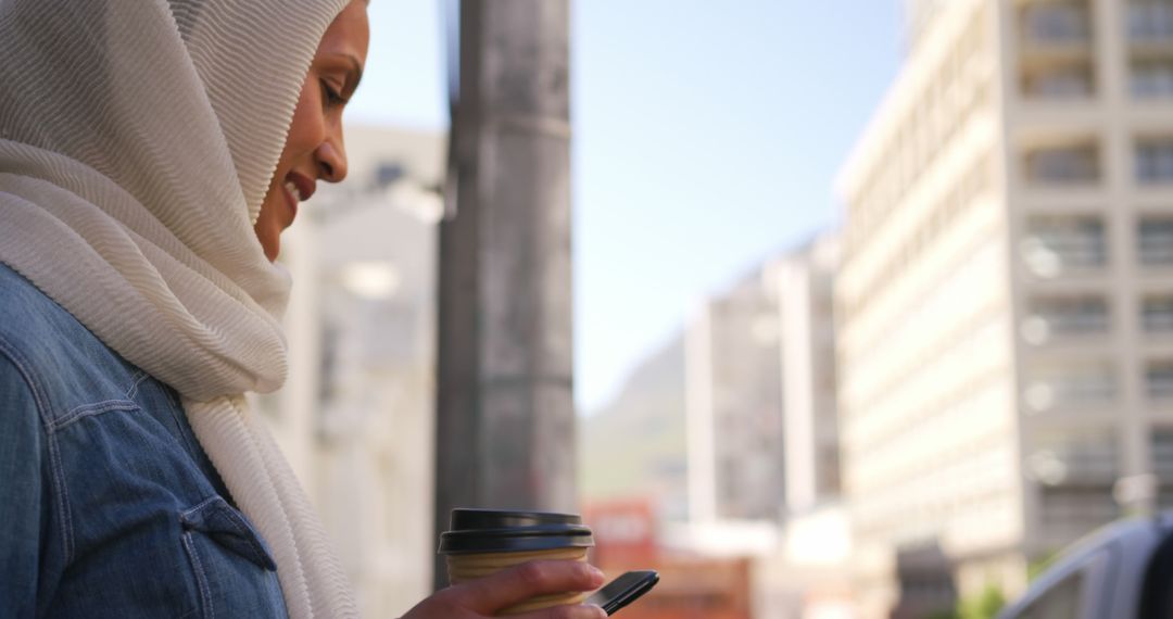 Muslim Woman Smiling While Using Smartphone on City Street - Free Images, Stock Photos and Pictures on Pikwizard.com