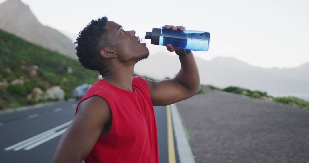 African american man drinking water while standing on the road - Free Images, Stock Photos and Pictures on Pikwizard.com