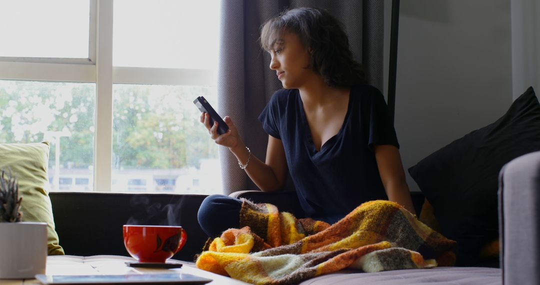 Young woman relaxing at home texting on smartphone by window - Free Images, Stock Photos and Pictures on Pikwizard.com