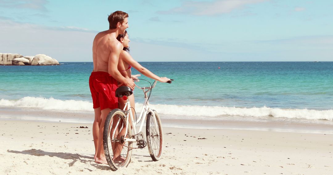 A couple shares a romantic bicycle lesson on a sunny beach, embodying adventure and togetherness. - Free Images, Stock Photos and Pictures on Pikwizard.com