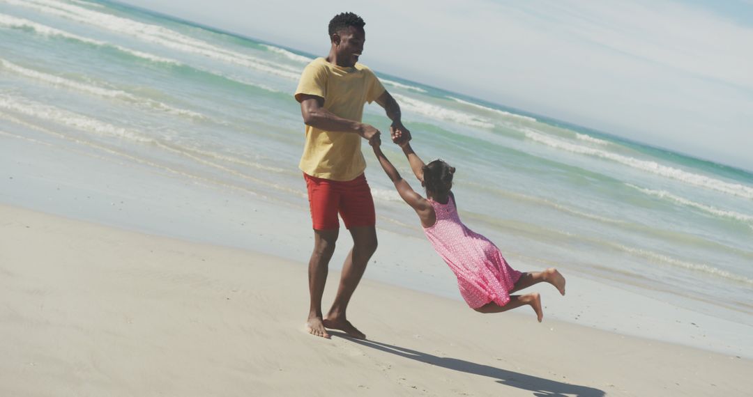 Father spinning daughter on sandy beach by the ocean - Free Images, Stock Photos and Pictures on Pikwizard.com