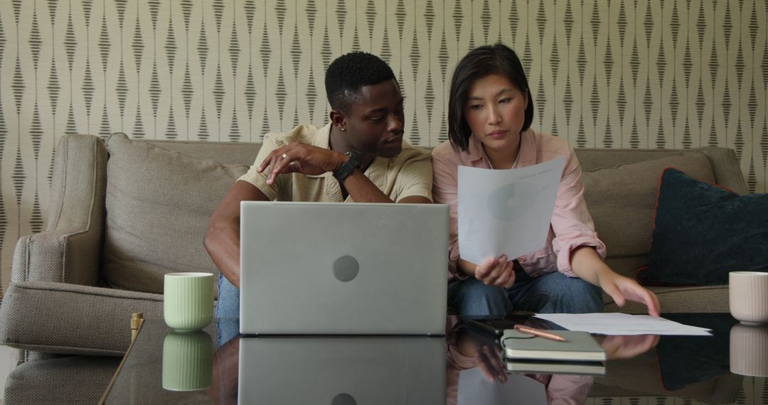 Diverse Colleagues Analyzing Documents with Laptop on Sofa