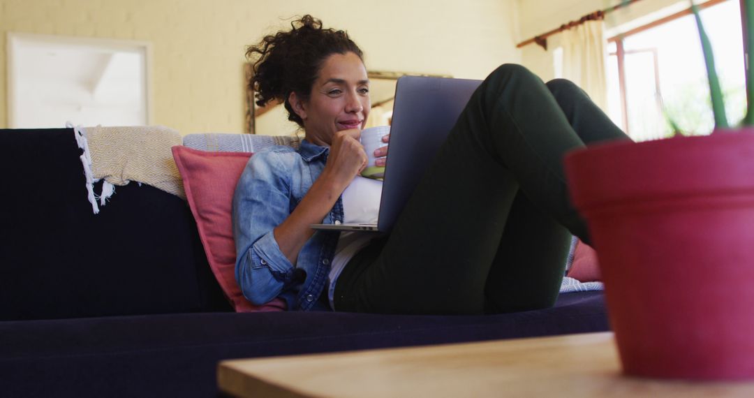 Woman Relaxing on Couch Working on Laptop with Coffee Mug - Free Images, Stock Photos and Pictures on Pikwizard.com