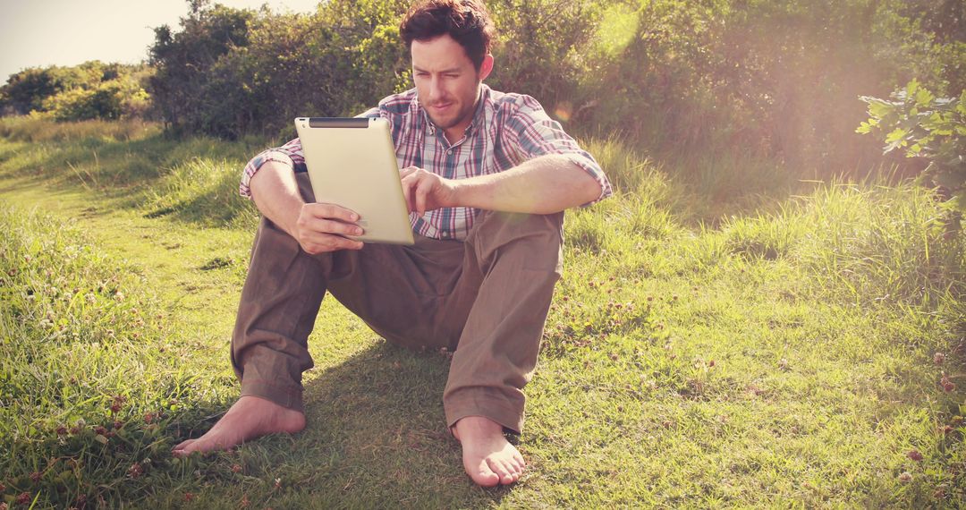 Man Sitting Outdoors on Grass Reading Tablet - Free Images, Stock Photos and Pictures on Pikwizard.com