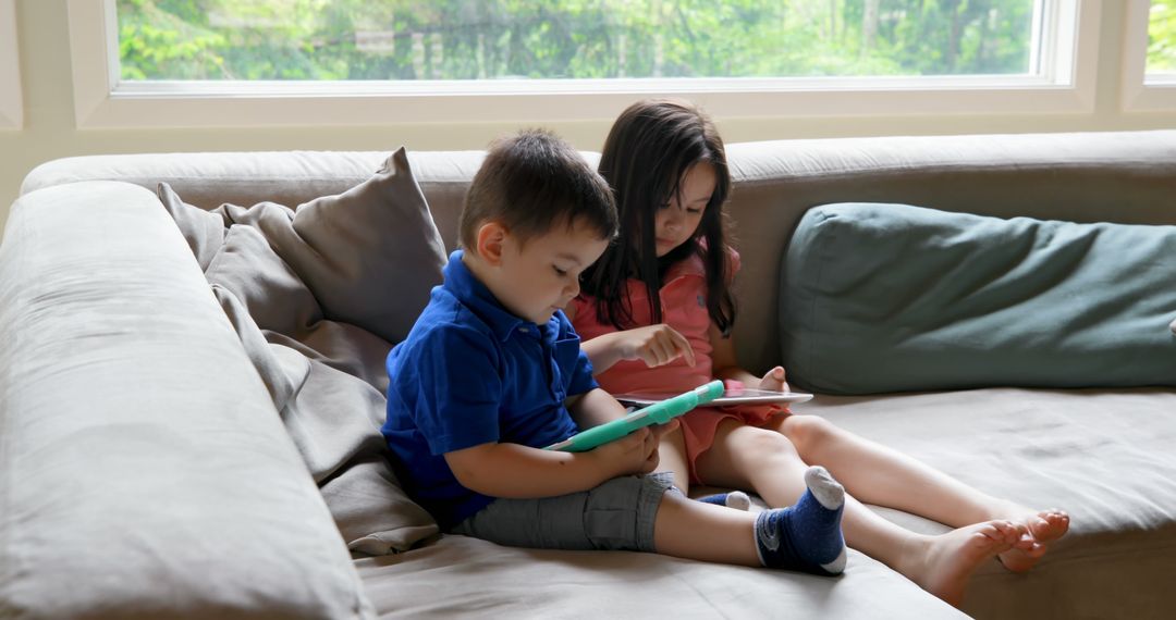 Children Using Tablets While Sitting on Sofa at Home - Free Images, Stock Photos and Pictures on Pikwizard.com