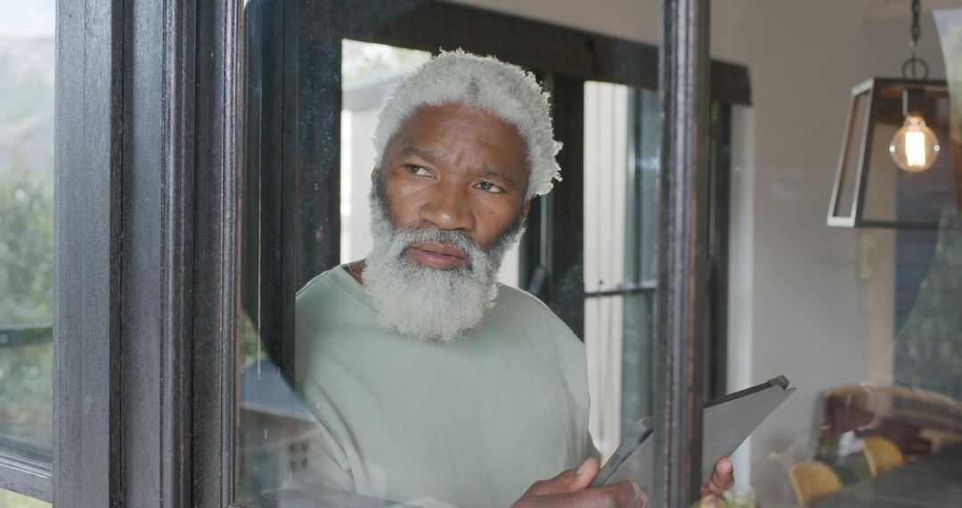 Senior Man Using Tablet Near Home Window with Relaxed Expression