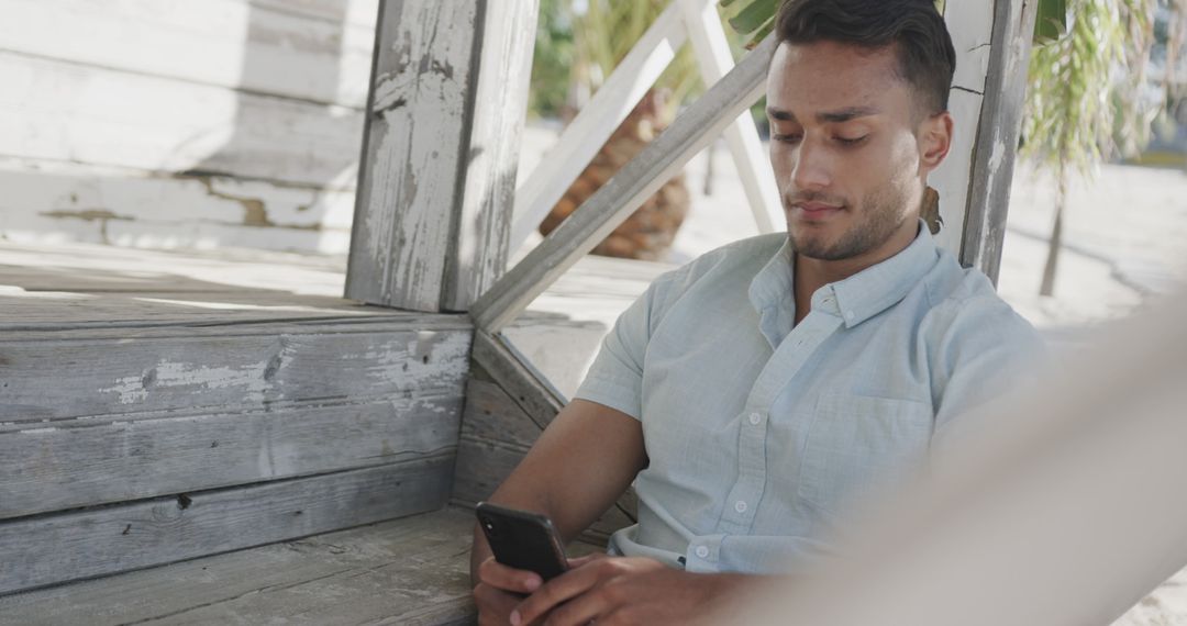 Man Relaxing and Using Smartphone in Wooden Structure Outdoors - Free Images, Stock Photos and Pictures on Pikwizard.com