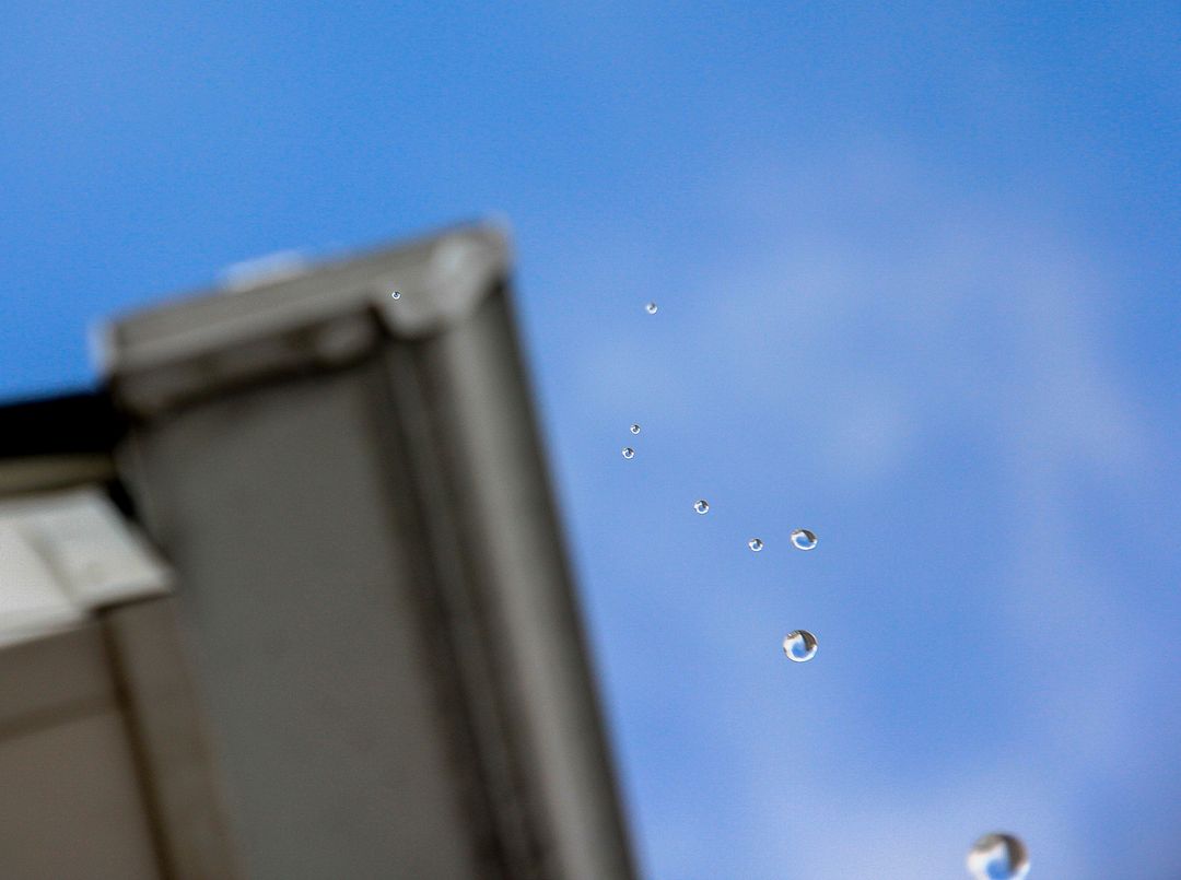 Close-up Raindrops Falling from Roof Against Blue Sky - Free Images, Stock Photos and Pictures on Pikwizard.com