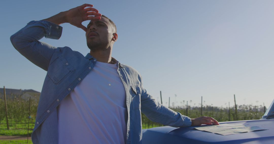 Man Shielding Eyes from Sun Standing by Blue Car in Field - Free Images, Stock Photos and Pictures on Pikwizard.com