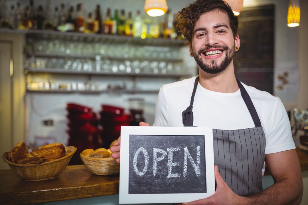 Cheerful Barista Holding Open Sign in Welcoming Cafe Environment