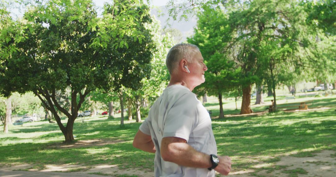 Senior Man Running in Park with Earbuds on Sunny Day - Free Images, Stock Photos and Pictures on Pikwizard.com