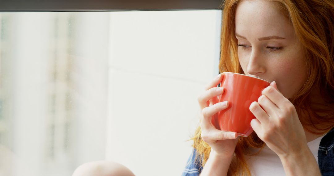 Redheaded Woman Sipping Hot Beverage by Window - Free Images, Stock Photos and Pictures on Pikwizard.com