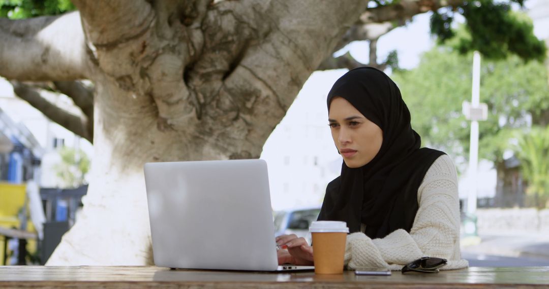 Focused Muslim Woman Working on Laptop in Outdoor Park - Free Images, Stock Photos and Pictures on Pikwizard.com