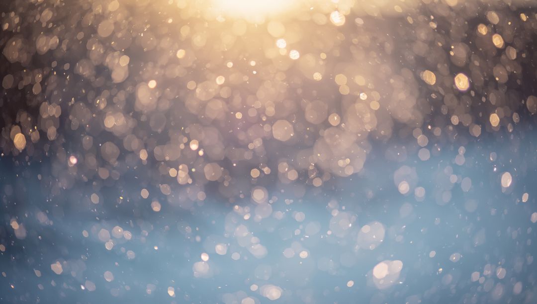 Sunlit bokeh particles glittering over blue snow blur with warm golden dreamy highlights