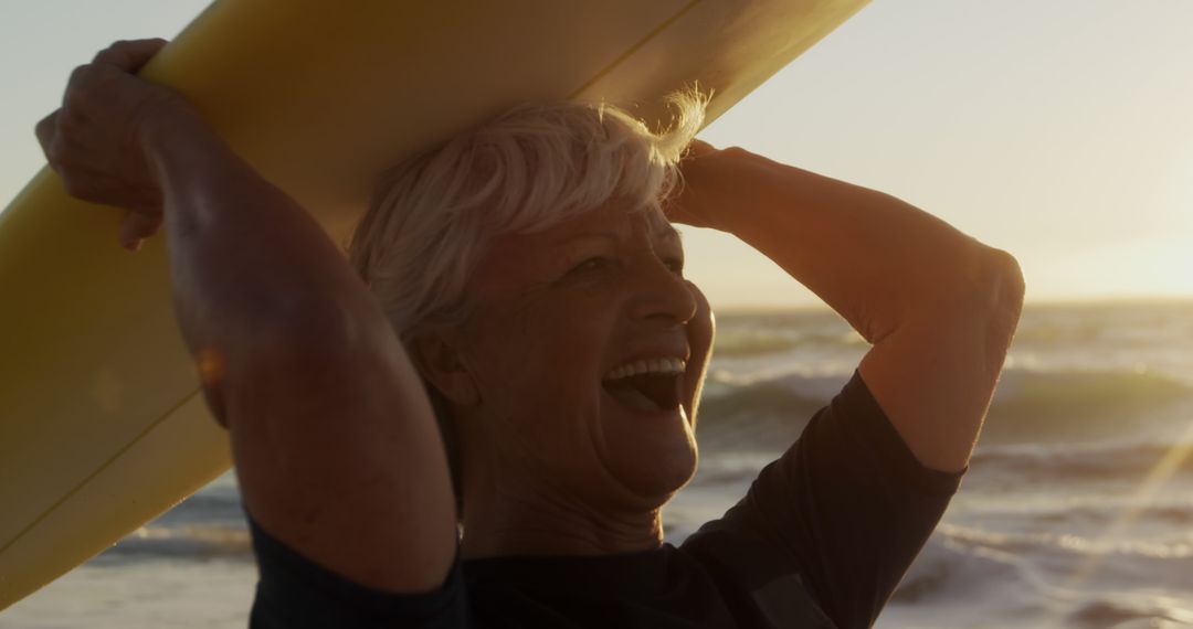 Joyful Senior Woman Carrying Surfboard at Sunset Beach - Free Images, Stock Photos and Pictures on Pikwizard.com