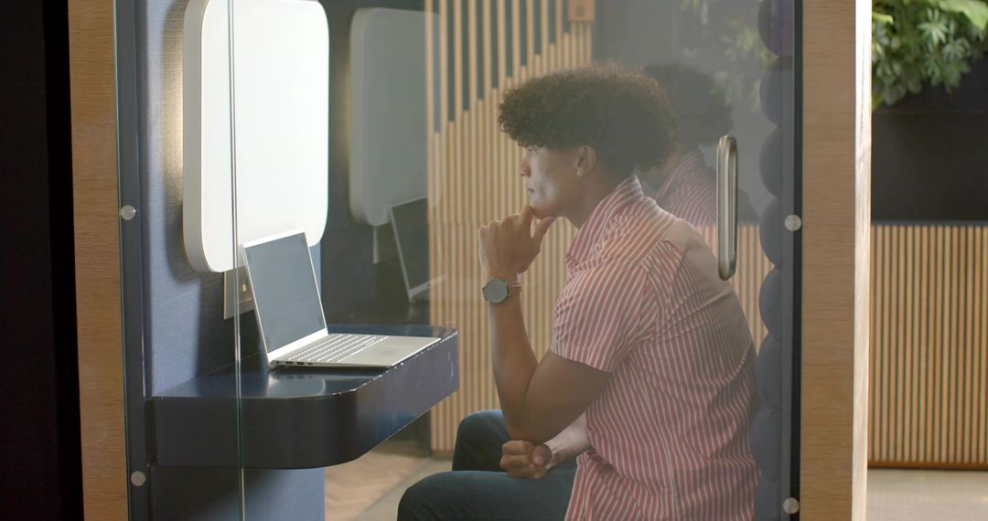 Young man working in glass booth with laptop, modern coworking private workspace