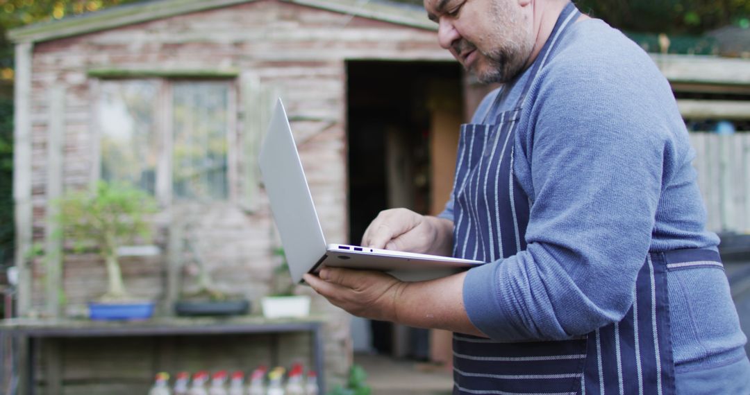 Bearded Man in Striped Apron Using Laptop Outdoors - Free Images, Stock Photos and Pictures on Pikwizard.com