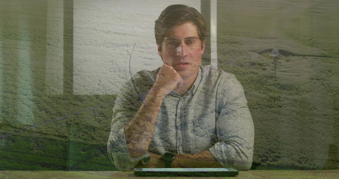 Contemplating businessman resting chin on fist at desk with tablet and landscape overlay