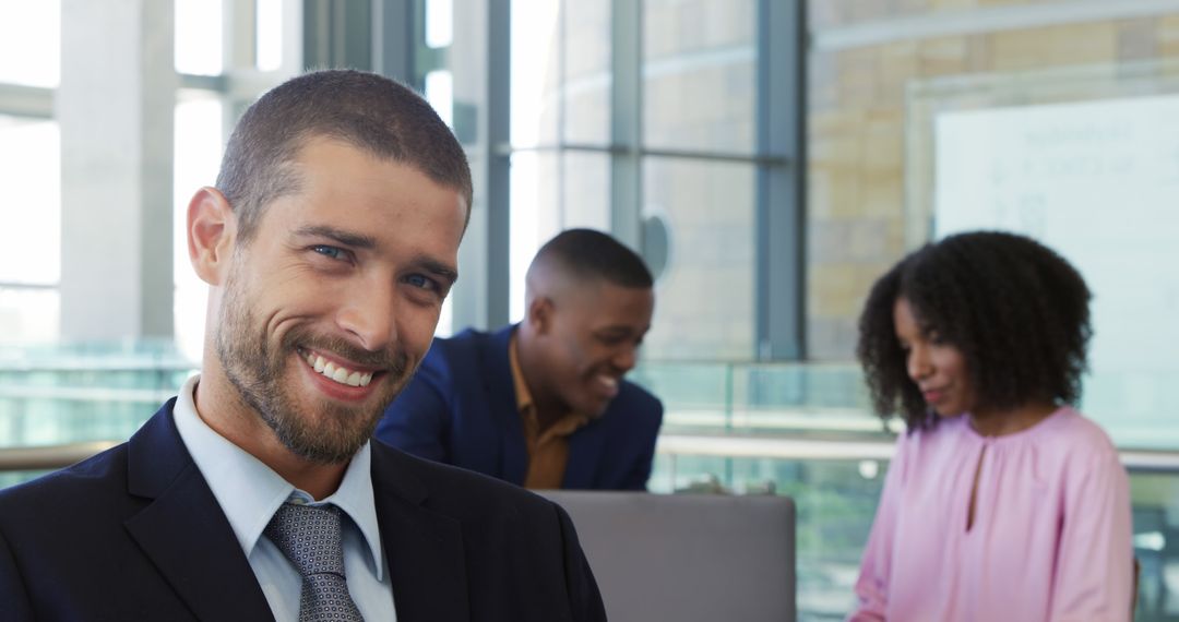 Confident Businessman Smiling in Modern Office with Colleagues in Background - Free Images, Stock Photos and Pictures on Pikwizard.com