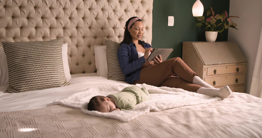 Mother Relaxing with Tablet Beside Sleeping Baby in Cozy Bedroom