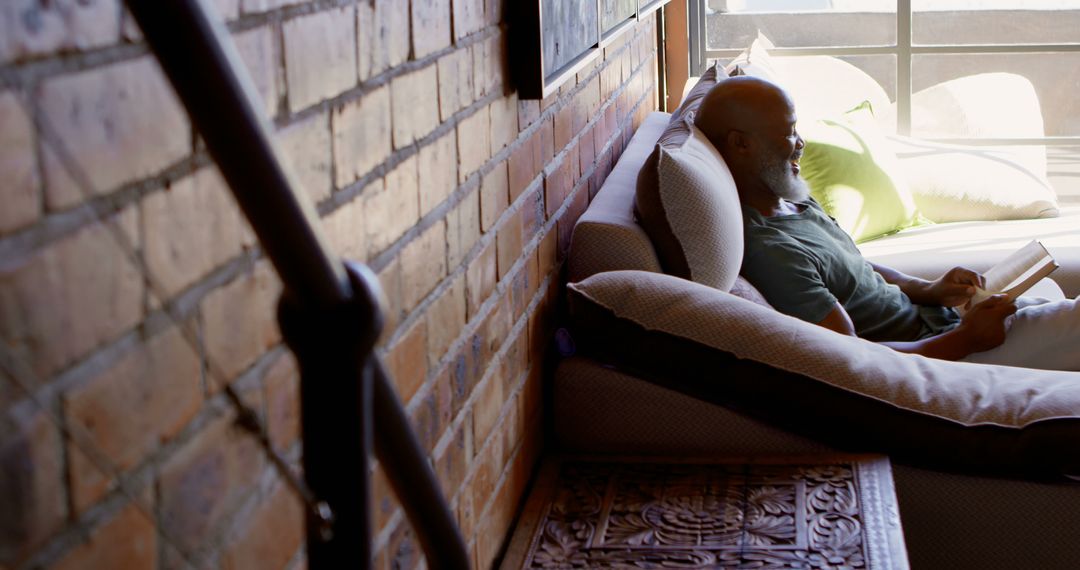 Relaxed Man Reading a Book on a Couch by a Window - Free Images, Stock Photos and Pictures on Pikwizard.com