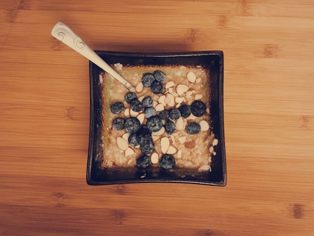 Serving warm oatmeal topped with fresh blueberries and sliced almonds in square ceramic bowl