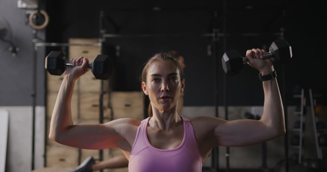 Focused Woman Lifting Dumbbells in Gym Environment
