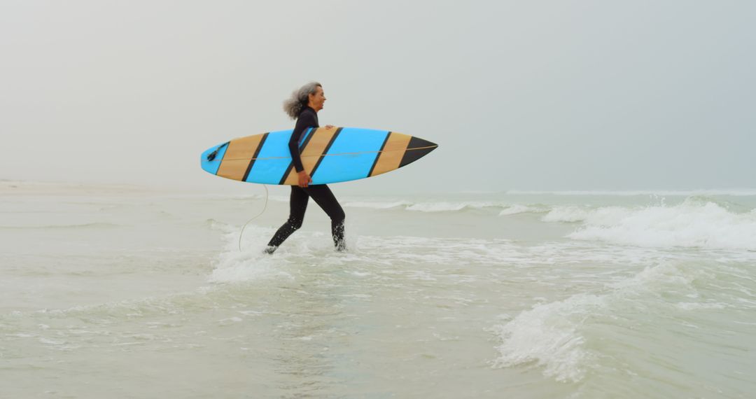 Senior Female Surfer Running with Board towards Ocean Waves