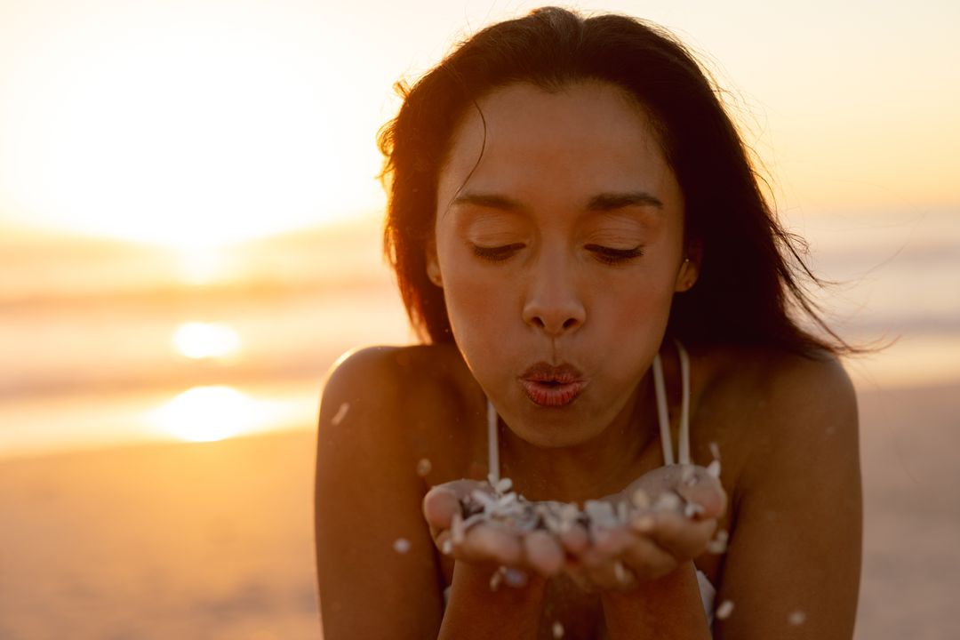 Young Woman Blowing Flower Petals on Beach at Sunset - Free Images, Stock Photos and Pictures on Pikwizard.com