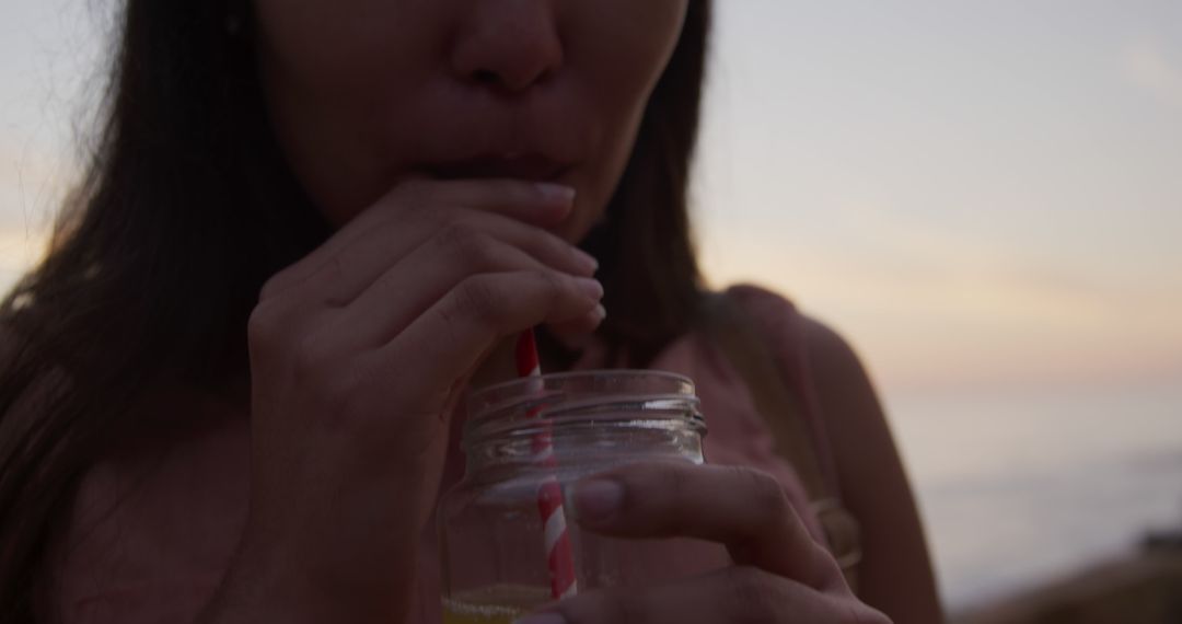 Woman Drinking Beverage with Red and White Straw at Beach Sunset - Free Images, Stock Photos and Pictures on Pikwizard.com