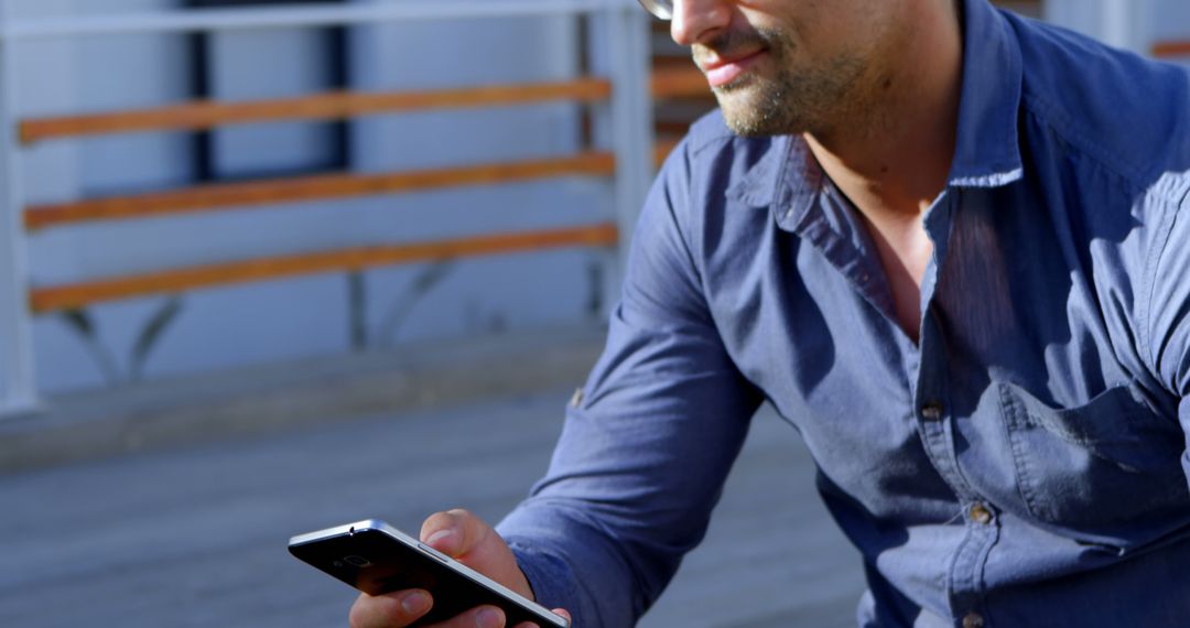 Man Using Smartphone in Sunlight Wearing Glasses and Casual Shirt - Free Images, Stock Photos and Pictures on Pikwizard.com