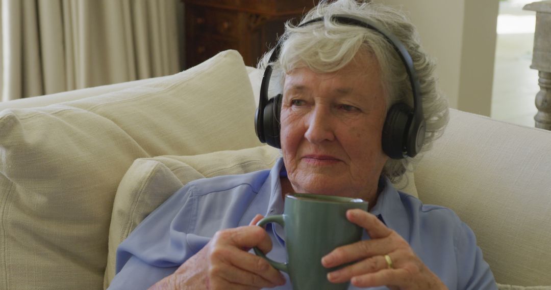 Caucasian senior woman wearing headphones listening to music while holding coffee cup at home - Free Images, Stock Photos and Pictures on Pikwizard.com
