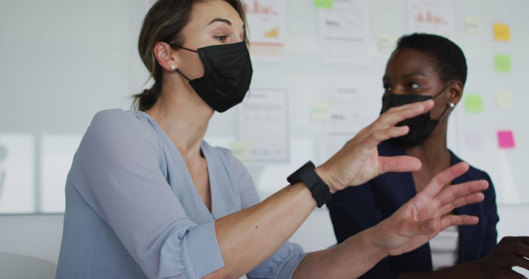 Businesswomen Discussing Project in Office Wearing Masks - Free Images, Stock Photos and Pictures on Pikwizard.com