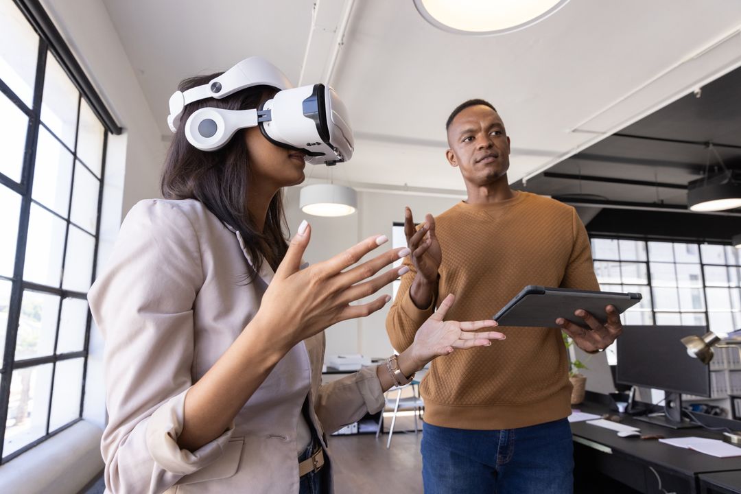 Diverse coworkers testing virtual reality headset and collaborating with tablet in modern office