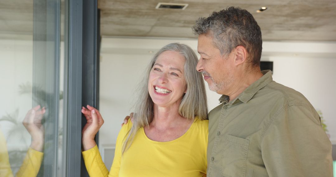 Senior Couple Smiling by Glass Door in Modern Home