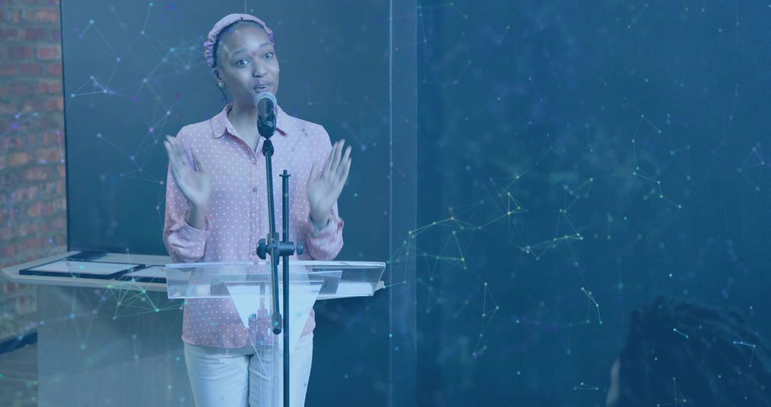 Woman delivering conference presentation at clear lectern while gesturing into microphone
