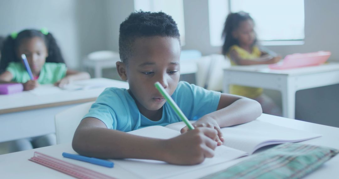 African American Boy Writing in Classroom Leaning Over Notebook Focusing on Learning