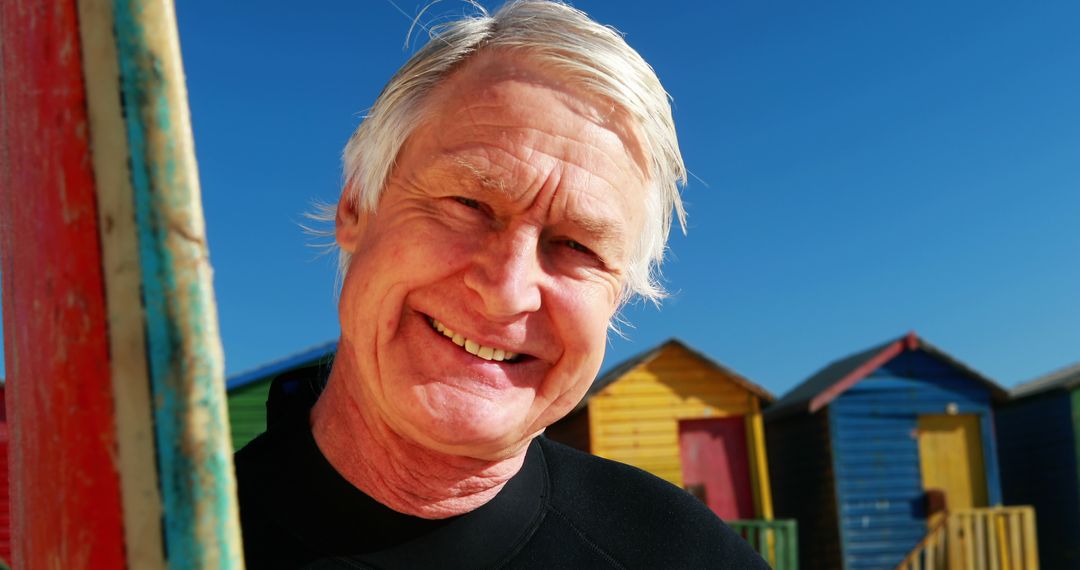 Smiling Senior Man in Front of Colorful Beach Huts on a Sunny Day - Free Images, Stock Photos and Pictures on Pikwizard.com