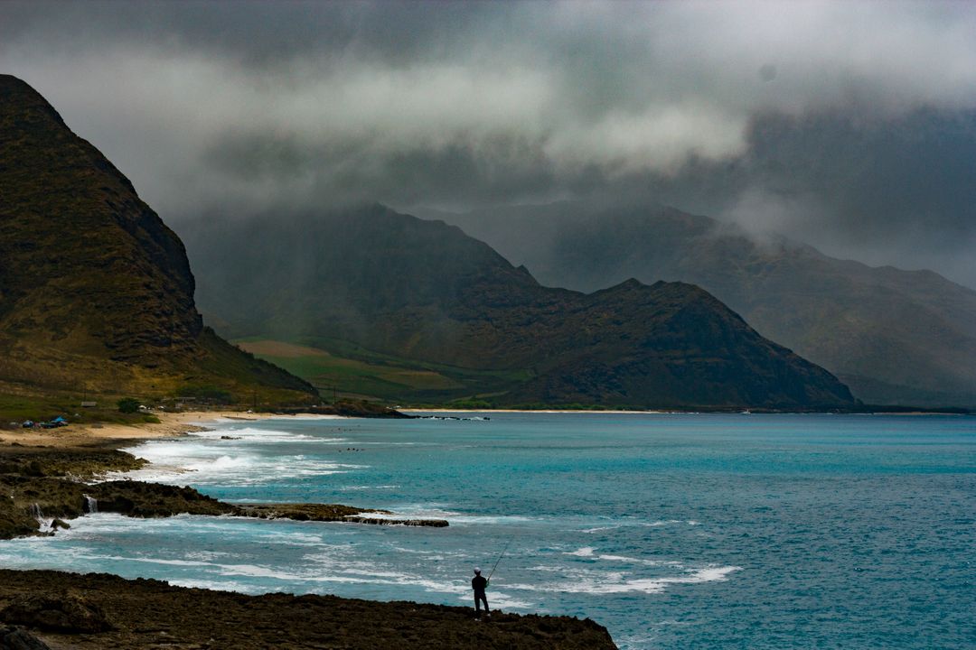 Solitary Fisherman by Rocky Ocean Landscape and Storm Clouds - Free Images, Stock Photos and Pictures on Pikwizard.com