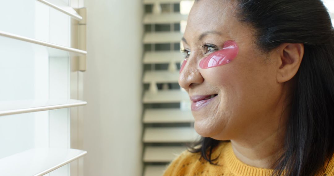Woman Relaxing by Window Wearing Pink Eye Patches at Home