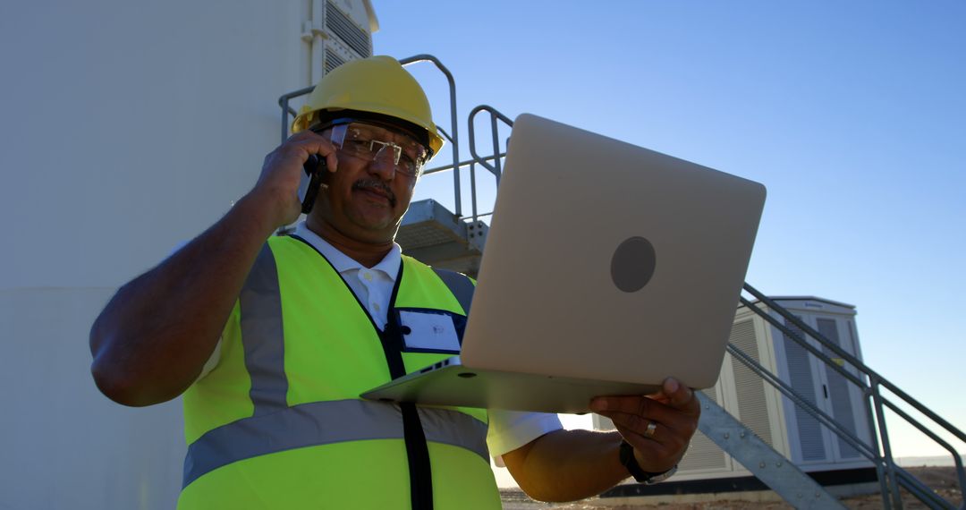 Construction Worker Holding Laptop and Talking on Phone at Site - Free Images, Stock Photos and Pictures on Pikwizard.com