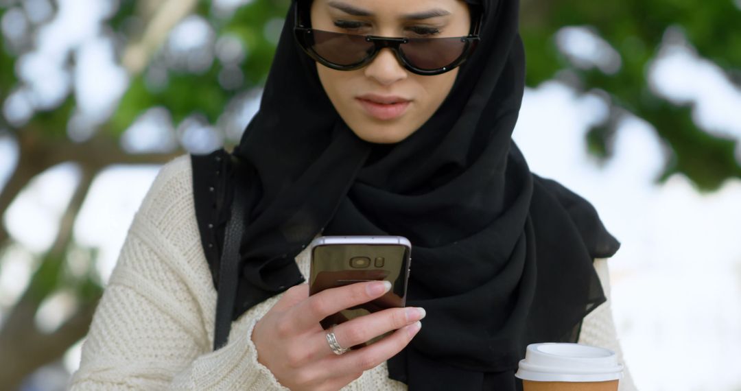 Confident Muslim Woman Using Smartphone Outdoors with Coffee - Free Images, Stock Photos and Pictures on Pikwizard.com