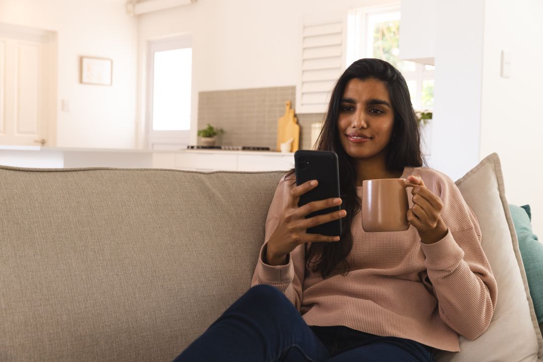 Relaxed Woman Enjoying Coffee While Using Smartphone on Sofa