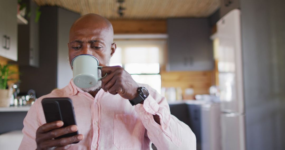 Mature Man Drinking Coffee and Browsing Smartphone in Modern Kitchen - Free Images, Stock Photos and Pictures on Pikwizard.com