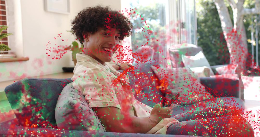 Smiling man relaxing on blue sofa holding remote amid confetti in bright modern lounge