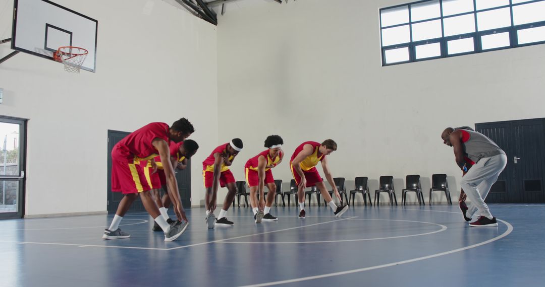 Diverse Basketball Team Stretching on Court with Coach Guidance